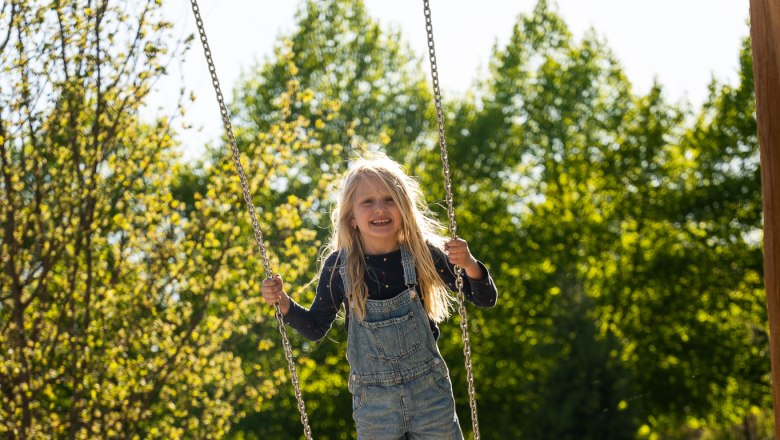 Starkl Erlebnisgarten, © starklfilm Ein Kind schaukelt fröhlich auf einem Spielplatz im Grünen.