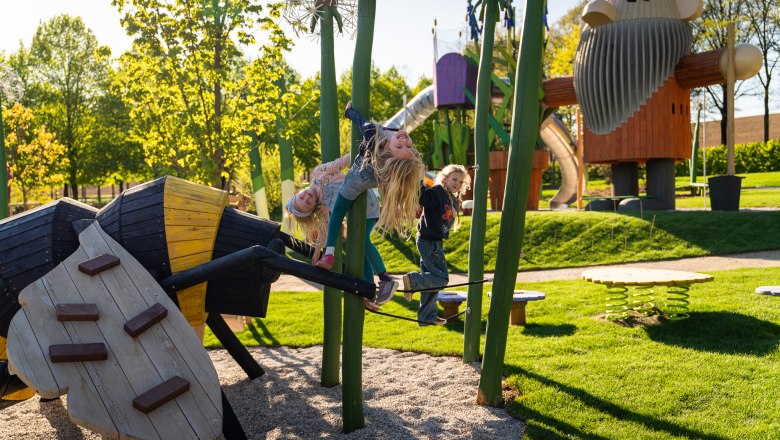 Starkl Erlebnisgarten, © starklfilm Kinder spielen auf einem Spielplatz mit großen Holzfiguren und Klettergeräten.