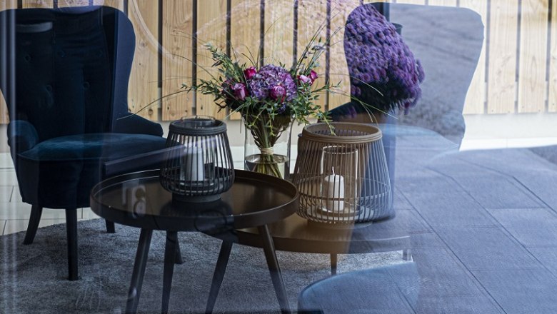 Stadthotel Gürtler Lobby, © Doris Schwarz-König Ein gemütlicher Loungebereich mit blauen Sesseln, einem Tisch mit Kerzen und einem Blumenstrauß, reflektiert in einer Glaswand.