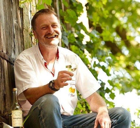 Wastlbauer, © Heckenbichler Mann sitzt draußen mit einem Glas Wein in der Hand, umgeben von grünen Pflanzen.