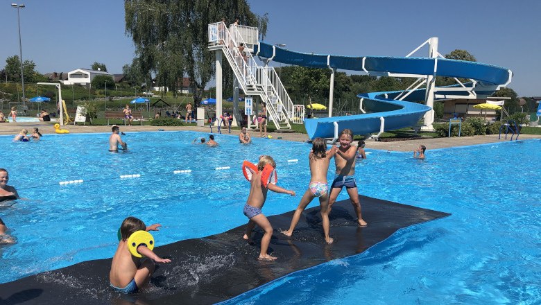 Kinder spielen im Freibad Neuhofen an der Ybbs auf einer schwimmenden Matte vor einer Wasserrutsche.