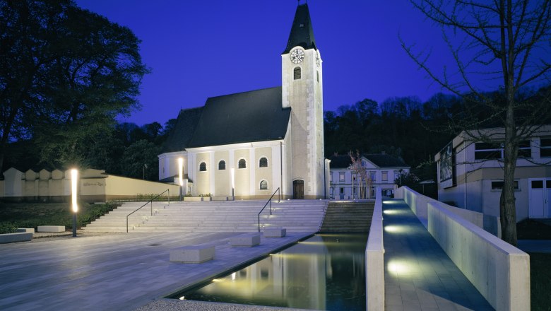 Abendaufnahme eines beleuchteten Kirchenplatzes mit Treppen und Wasserbecken in Ernsthofen.