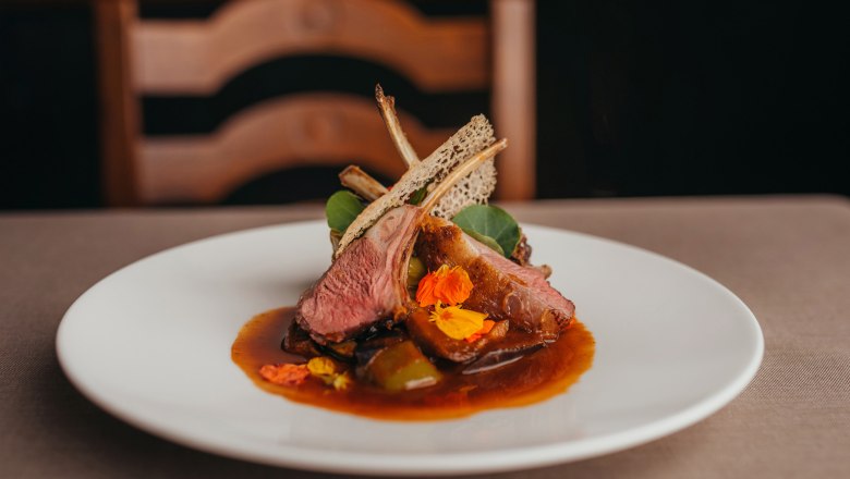 Gourmetgericht mit Lamm, Minipaprika, Brunnenkresse und Jus auf weißem Teller.