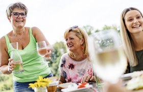 Drei Frauen lachen und genie&szlig;en ein Getr&auml;nk im Freien.