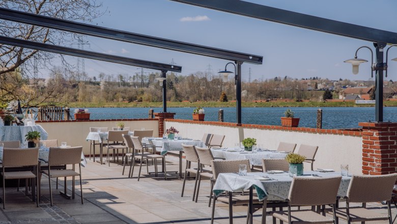 Terrasse mit Tischen und St&uuml;hlen, Blick auf einen Stausee und umliegende Landschaft.