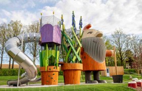 Ein fantasievoller Spielplatz mit einen gro&szlig;en Holzfiguren und einer Rutsche.