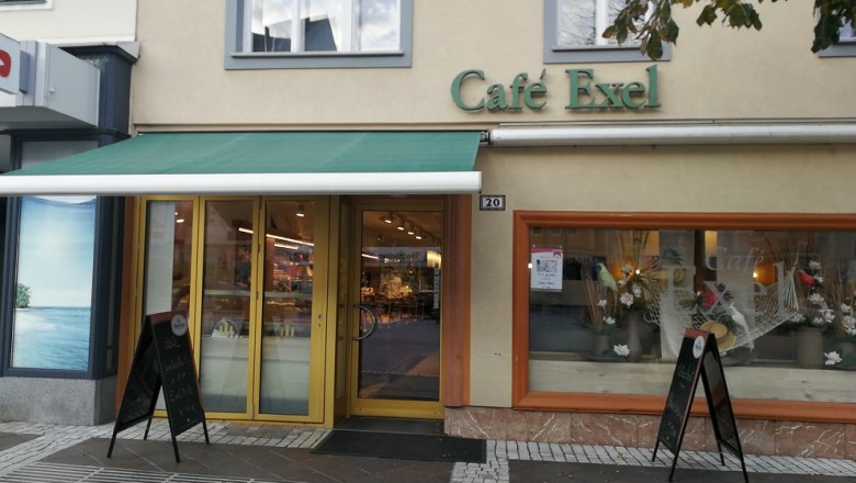 Au&szlig;enansicht des Caf&eacute; Exel mit gr&uuml;ner Markise und Schaufensterdekoration.