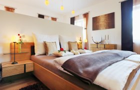 Gemütliches Schlafzimmer mit Doppelbett, dekoriert mit Kissen und Rosen, Holzmöbeln und sanfter Beleuchtung.