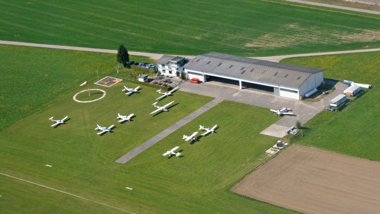 Luftaufnahme eines kleinen Flugplatzes mit mehreren geparkten Flugzeugen und einem Hangar.
