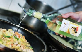 Eine Hand gießt Most aus einer Flasche in eine Pfanne mit Gemüse.