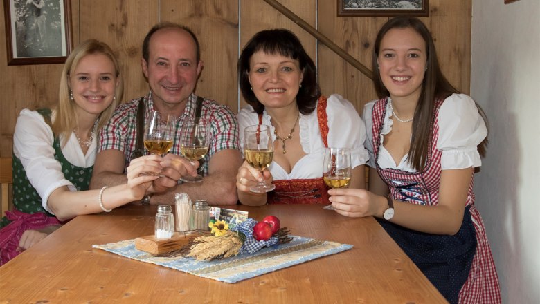 Eine Familie in traditioneller Kleidung stößt mit Weingläsern an einem Holztisch an.