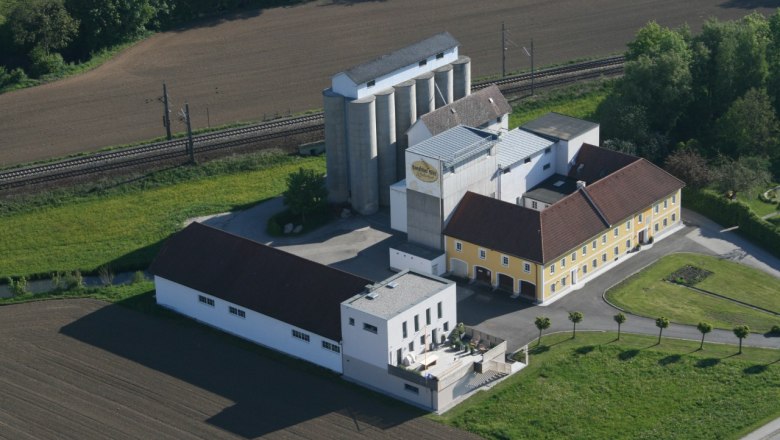 Luftaufnahme der Rosenfellner Mühle mit Gebäuden und Silos, umgeben von Feldern und Bahngleisen.
