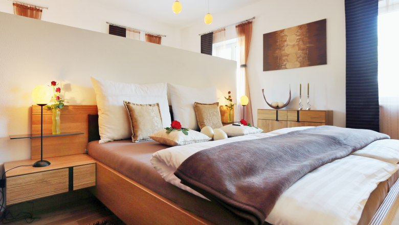Gemütliches Schlafzimmer mit Doppelbett, dekoriert mit Kissen und Rosen, Holzmöbeln und sanfter Beleuchtung.