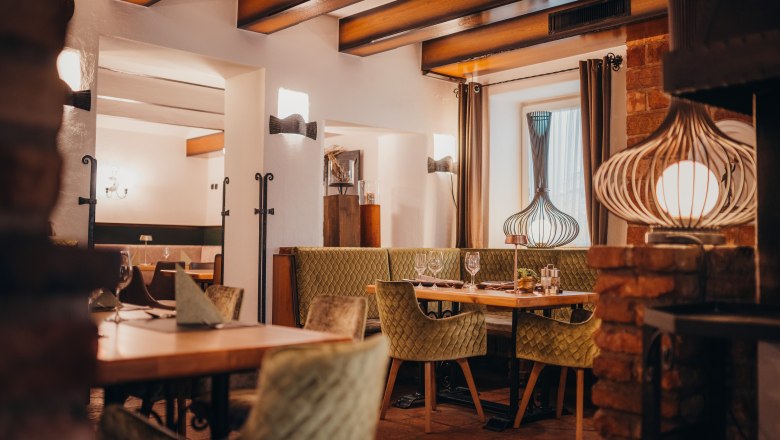 Gemütliches Restaurant mit Holzbalken, grünen Polsterstühlen und dekorativen Lampen.