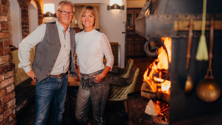 Ein Mann und eine Frau stehen lächelnd in einem gemütlichen Raum mit Kamin.