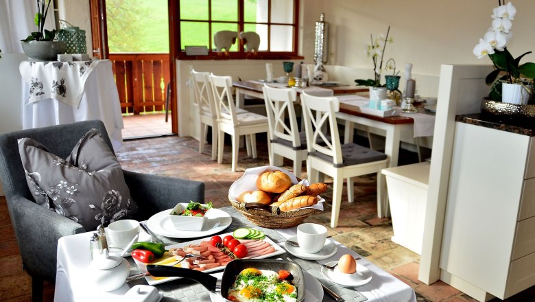 Fr&uuml;hst&uuml;ckstisch in einem gem&uuml;tlichen Esszimmer mit Blick auf eine gr&uuml;ne Landschaft.