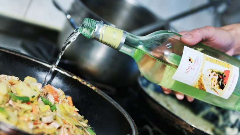 Eine Hand gießt Most aus einer Flasche in eine Pfanne mit Gemüse.