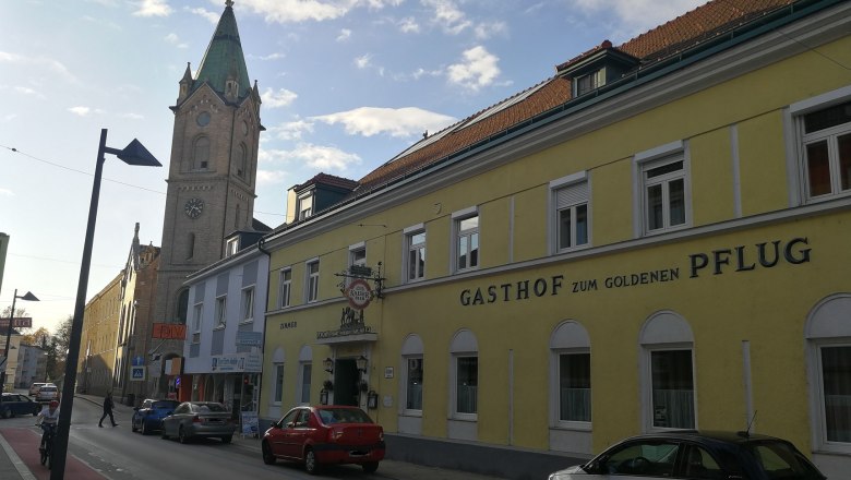 Stra&szlig;enszene mit gelbem Geb&auml;ude 'Gasthof zum goldenen Pflug' und Kirchturm im Hintergrund.