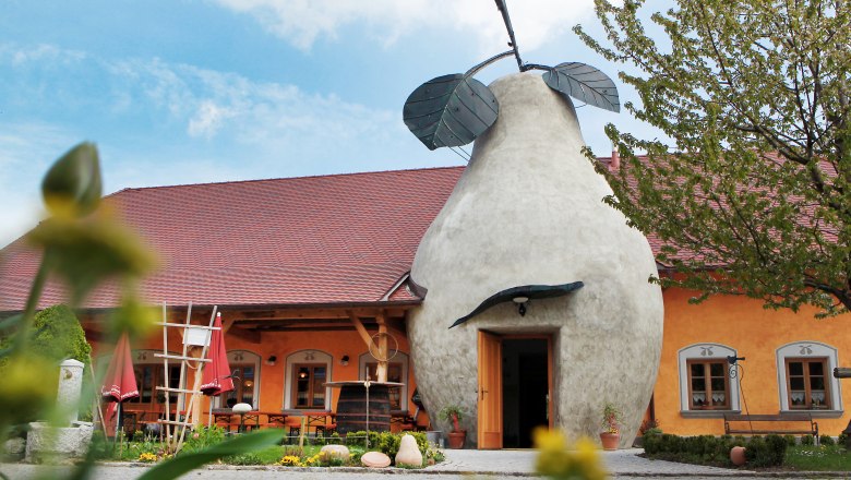 Gebäude mit birnenförmigem Eingang und rotem Dach, umgeben von Pflanzen.