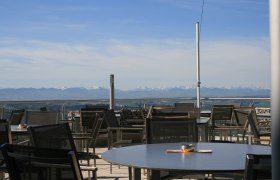 Terrasse mit Tischen und Stühlen, im Hintergrund Alpenpanorama.