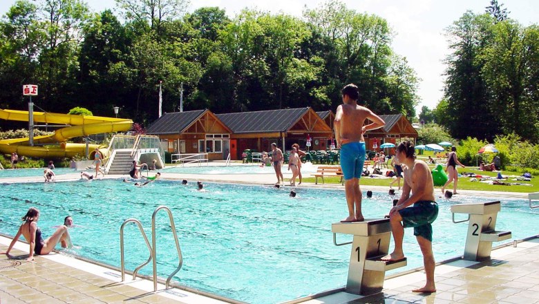 Freibad mit Schwimmern und Rutsche im Hintergrund.