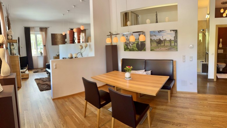 Modern eingerichtetes Wohnzimmer mit Esstisch, St&uuml;hlen und Dekorationen, darunter Bilder von Strau&szlig;en.