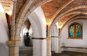 Gewölbekeller mit Backsteinbögen und buntem Glasfenster.