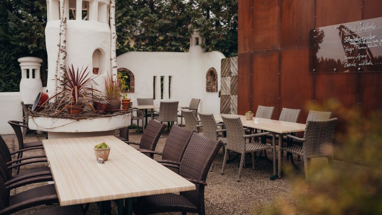 Ein gemütlicher Gastgarten mit Holztischen, geflochtenen Stühlen und dekorativen Pflanzen in einem weißen Turm.