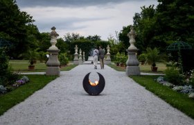 Ein Kiesweg im historischen Hofgarten des Stifts Seitenstetten mit Skulpturen und Pflanzen, im Vordergrund eine Feuerstelle.