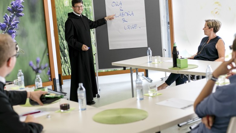 Ein Seminar im Stift Seitenstetten mit einem Vortragenden in Mönchskleidung, der auf ein Flipchart zeigt. Teilnehmer sitzen an Tischen.