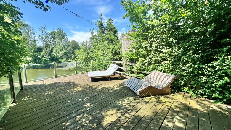 Holzterrasse mit Liegest&uuml;hlen und Blick auf den Fluss Ybbs, umgeben von B&auml;umen.