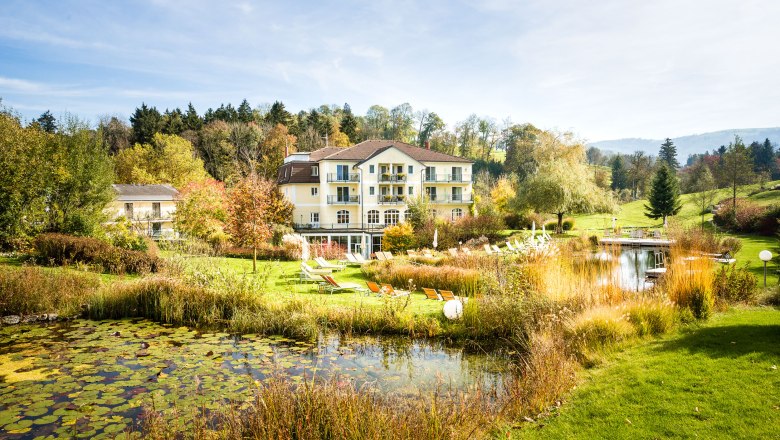 Ein Hotel inmitten einer grünen Landschaft mit Teich und Liegestühlen.
