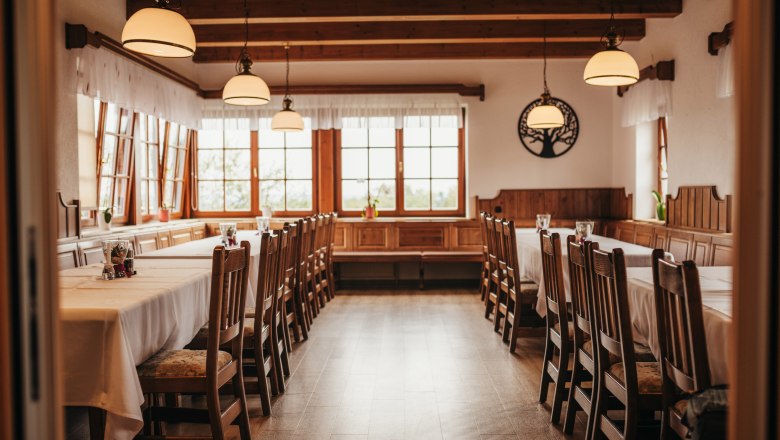 Gem&uuml;tlicher Gastraum mit Holzm&ouml;beln und gro&szlig;en Fenstern.