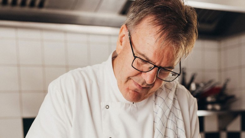 Ein Koch in wei&szlig;er Uniform arbeitet konzentriert in einer K&uuml;che.