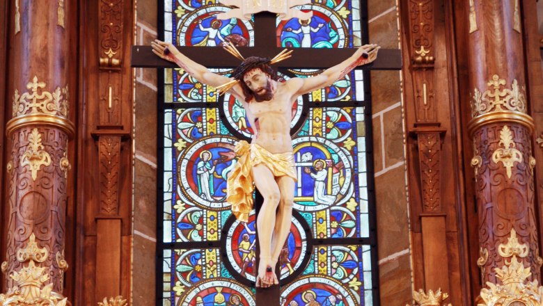 Kruzifix vor einem bunten Kirchenfenster in der Stiftskirche Ardagger.