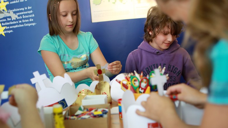 Kinder basteln an einem Tisch mit Papier und Scheren.