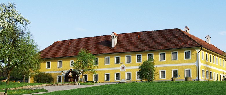 Gro&szlig;es gelbes Geb&auml;ude mit rotem Dach in l&auml;ndlicher Umgebung.