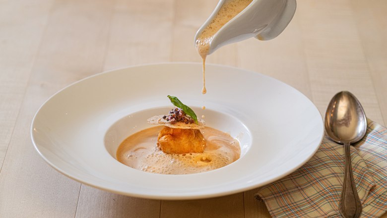 Krebssuppe wird in einen Teller gegossen, dekoriert mit einer Teigkugel und Kräutern.