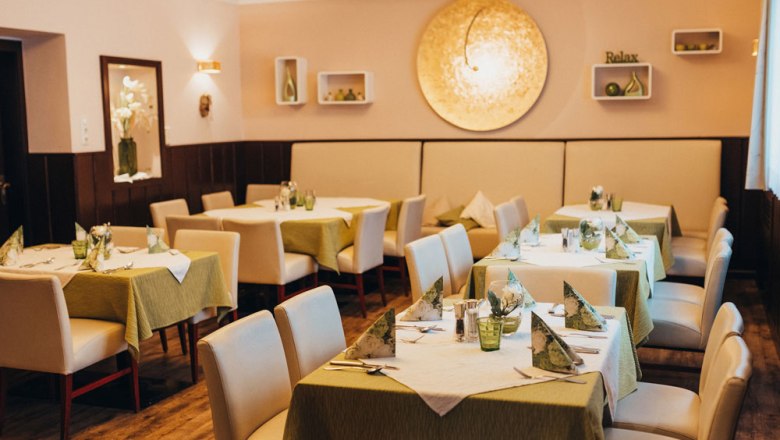 Elegantes Restaurant mit gedeckten Tischen und gr&uuml;nen Tischdecken.