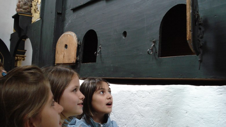 Drei Kinder betrachten neugierig eine Wand mit kleinen Türen.