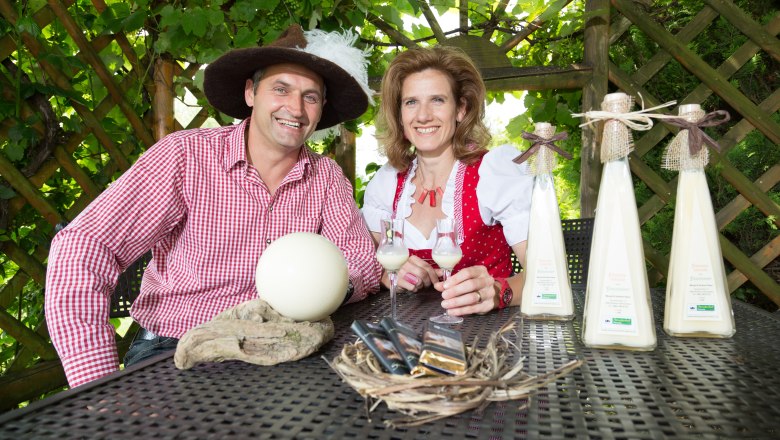 Ein Mann und eine Frau in traditioneller Kleidung sitzen an einem Tisch mit Straußeneiern und Likörflaschen.