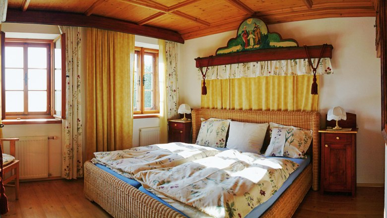 Gem&uuml;tliches Schlafzimmer mit Holzm&ouml;beln und Doppelbett, dekoriert mit floralen Mustern und gelben Vorh&auml;ngen.