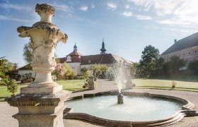 Brunnen im Garten des Stifts Seitenstetten mit barocker Architektur im Hintergrund.