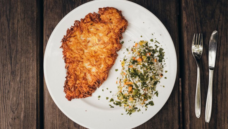 Ein Teller mit einem Kartoffel-Schnitzel und Reisgemüse auf Holztisch.