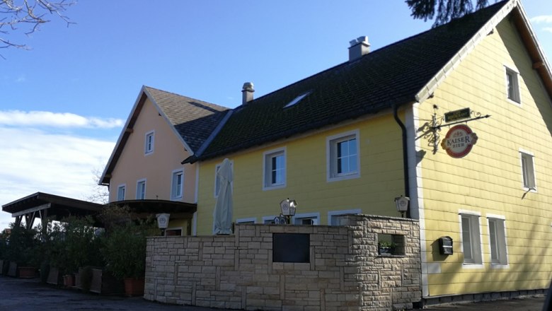 Gelbes Landgasthaus mit Kaiser Bier Schild und Sonnenschirm im Vordergrund.
