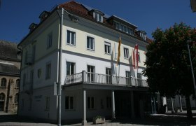 Gebäude des Stadtamts St. Valentin mit Flaggen und Baum im Vordergrund.